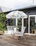 Patio with wicker chairs, floral umbrella, potted cacti, and ivy-covered black brick house.