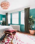 Bedroom with teal walls, a navy bed, white bedding, pink chandelier, and a red patterned rug.