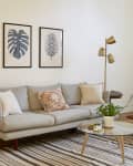 Living room with gray sofa, brown chair, striped rug, gold floor lamp, and framed leaf prints on the wall.