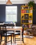 Dining room with black and white table, black chairs, yellow bookshelf, and potted plants near a window.