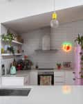 Modern kitchen with white subway tiles, pink fridge, neon peach sign, and colorful decor.