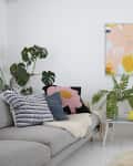 Modern living room with gray sofa, colorful cushions, abstract wall art, and lush green plants.