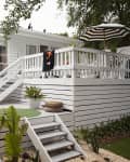 Modern patio with white deck, lounge chairs, fringed umbrella, potted plants, and striped parasol.