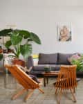 Living room with gray sofa, wooden chairs, large potted plants, and abstract wall art.