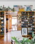 Living room with wooden shelves filled with plants, books, and decor, leading to a dining area with a table and chairs.