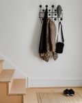 Wooden staircase next to a coat rack with jackets and a bag, shoes on a mat by the door.
