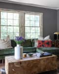 Living room with green velvet sofa, wooden coffee table, floral cushions, and a ladder shelf beside a doorway to the kitchen.