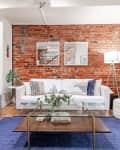 Living room with exposed brick wall, white sofa, blue rug, glass coffee table, and modern decor elements.