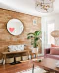 Living room with pink sofa, midcentury coffee table, exposed brick wall, and round mirror