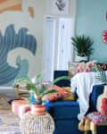 Living room with sun and wave mural, colorful cushions, blue sofa, and potted plants on a patterned rug.