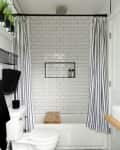 Bathroom with white subway tiles, striped shower curtain, wooden bath tray, and potted plants on a shelf.