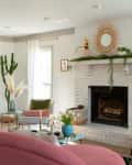 Living room with white brick fireplace, pink sofa, green plants, and modern decor.