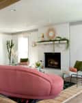 Living room with pink sofa, white brick fireplace, green plants, and French doors.