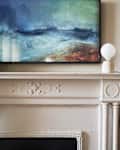 Painting of ocean waves above a white ornate fireplace with a round lamp.