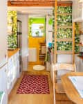 Cozy kitchen with wooden countertops, green leaf wallpaper, ladder, red rug, and dining table with pink flowers.