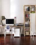 Home office with a wooden desk, computer, desk lamp, bookshelves, and a white chair on a wooden floor.