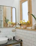 Bathroom with white subway tiles, large mirror, vessel sink, potted plants, and decorative yellow flowers on a wooden shelf.