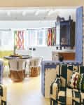 Colorful living room with patterned armchairs, vibrant curtains, round dining table, and eclectic decor.