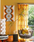 Retro living room with orange walls, patterned curtains, two round chairs, abstract art, and a potted plant by the window.