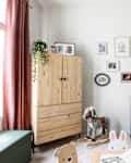 Nursery with a round black crib, colorful wall art, wooden wardrobe, rocking horse, and pink curtains.
