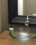 Bathroom vanity with glass vessel sink, black framed mirror, beige towel, and soap dispenser.