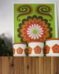 Retro kitchen decor with green and orange floral canisters, leafy plant, and a vibrant wall art piece above wooden cabinets.
