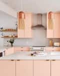 Modern kitchen with pink cabinets, white countertops, copper pendant lights, and plants on the island.