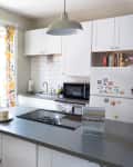 Bright kitchen with fruit-patterned curtains, white cabinets, a fridge with magnets, and a countertop stove.