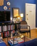 Cozy living room with blue walls, bookshelves, a TV, patterned chairs, and decorative plates on the wall.