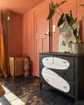 Coral-painted room with a black and white dresser, potted plant, yellow curtains, and a vintage crate.