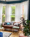 A beautiful living room decorated with suede couches in forest green and pink, a round marbled table, a rug, a round blue suede ottoman, and house plants at the corner