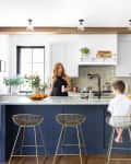Woman and two children in a modern kitchen with a navy island, white cabinets, and gold wire bar stools.