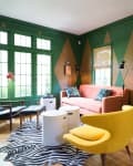 Living room with green walls, pink sofa, yellow chair, zebra rug, and crow artwork above a green fireplace.