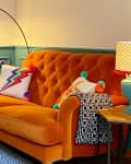 Orange tufted sofa with colorful pillows, blue lamp, and chevron shade in a room with teal wainscoting and wooden floor.