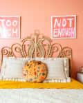 Bohemian bedroom with ornate headboard, coral walls, white bedding, yellow throw, and two lamps on white nightstands.