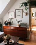 Cozy living room with a white sofa, wooden dresser, hanging plants, framed art, and a Marshall speaker.