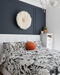 Bedroom with black and white floral bedding, orange pillow, dark accent wall, and white feather wall decor.