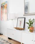 Entryway with a white console, potted plant, framed art, woven basket, and abstract wall painting.