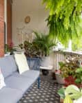 Cozy balcony with blue sofa, colorful cushions, potted plants, and hanging ferns.