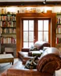 Cozy living room with leather chairs, bookshelves, and French doors, featuring a fireplace and decorative items.