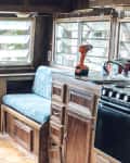 Wood-paneled RV kitchen with blue cushioned bench, stove, and tools on counter.