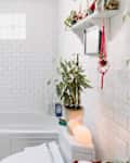 Bright bathroom featuring a white tub, shower curtain, potted plants, and decorative shelf with items.