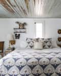 Cozy bedroom with patterned bedding, rustic wood ceiling, wall art, and decorative masks above the bed.