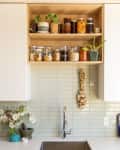 Modern wooden open shelving above a kitchen sink and backsplash filled with jars of dried goods