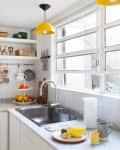 Bright kitchen with yellow pendant lights, fruit bowls, and a sink by a large window.