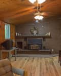 Wood-paneled living room with brick fireplace, ceiling fan, and vintage furniture.