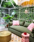 Green outdoor patio with a sofa, pink cushions, round gold table, and striped yellow umbrella.