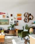 Living room with mustard sofa, green armchair, wall art, plants, and wooden furniture.