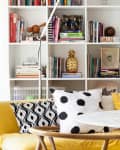 Yellow sofa with polka dot pillows, round marble table, and bookshelves filled with colorful books and decor items.