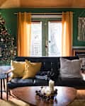 Living room with Christmas tree, black sofa, yellow curtains, and macramé wall hanging.